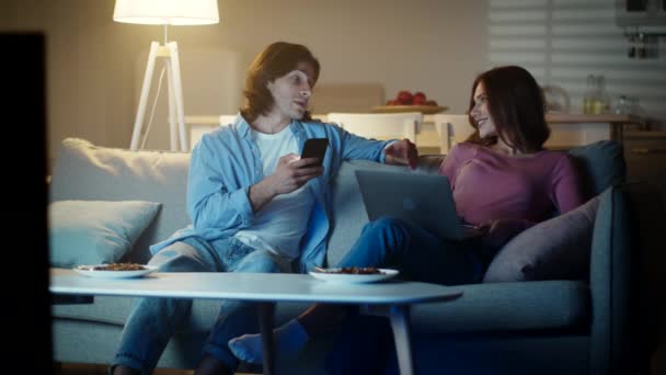 Jong stel brengen tijd samen, man browsen op smartphone en vrouw werken op laptop in de avond thuis — Stockvideo