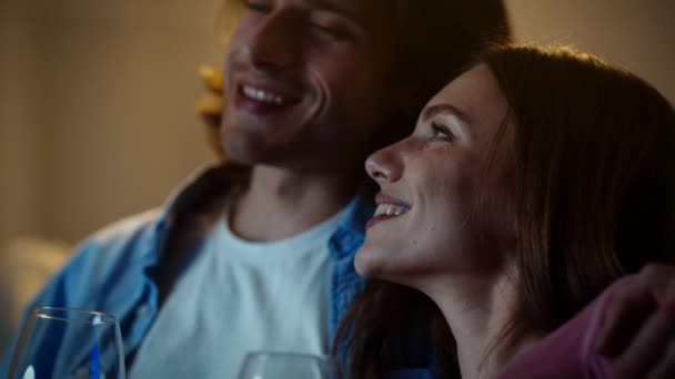 Закрыть портрет счастливых супругов, смотрящих телевизор вместе, улыбающихся друг другу и щёлкающих бокалами вина — стоковое видео