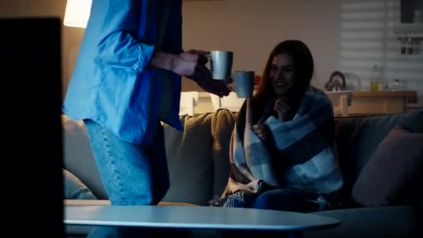 Zmrzlá žena sedící zabalená v kostkovaném kostýmu, její starostlivý manžel přinesl dva páry čaje a posadil se vedle ní — Stock video