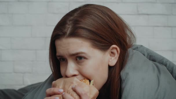 Depressieve jonge vrouw eet hamburger om zichzelf te troosten thuis — Stockvideo
