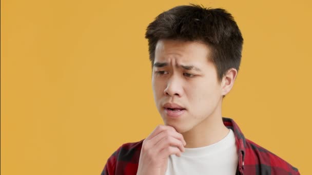 Азиатский парень думает о проблемах и хмурясь над желтым фоном — стоковое видео