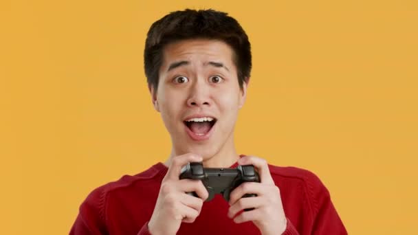 Χαρούμενος Ασιάτης που παίζει βιντεοπαιχνίδι γιορτάζοντας τη νίκη επί του κίτρινου φόντου — Αρχείο Βίντεο