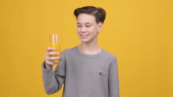 Menino adolescente bebendo suco de laranja e gestionando polegares para cima, fundo amarelo — Vídeo de Stock