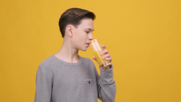 Adolescent garçon boire orange jus sourire à caméra, jaune fond — Video