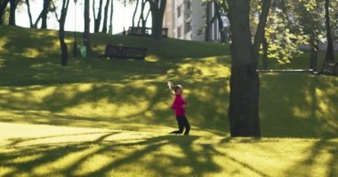 Parlak pembe ceketli genç sarışın bayan boş şehir parkında tek başına koşuyor, sabah koşusu antrenmanı yapıyor.