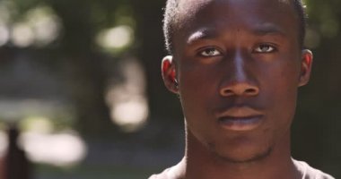 Genç, ciddi bir Afrikalı Amerikalının portresi. Kameraya bakıyor, dışarıda poz veriyor, yavaş çekim yapıyor.