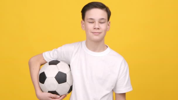Teenager Boy Posing Holding μπάλα ποδοσφαίρου στέκεται πάνω από κίτρινο φόντο — Αρχείο Βίντεο