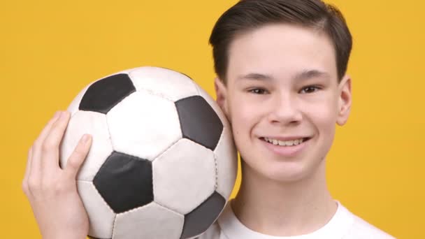 Ευτυχισμένος έφηβος αγόρι κρατώντας μπάλα Posing πάνω από κίτρινο φόντο — Αρχείο Βίντεο