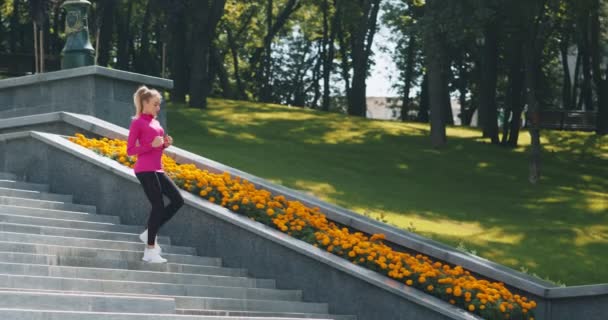 Millennial blonde dame in sportkleding loopt de stad trap af in de ochtend, uit te werken in het openbaar park, tracking shot — Stockvideo