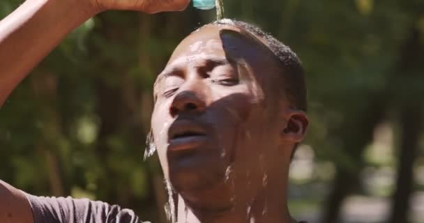 Ritratto ravvicinato di un giovane afroamericano surriscaldato che versa acqua sulla testa, che si allena all'aperto nel parco urbano — Video Stock