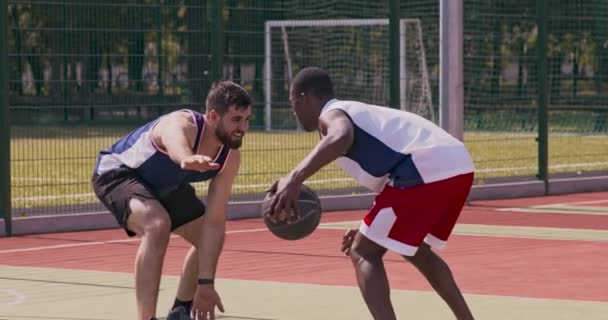 Jovens jogadores de basquete afro-americanos e caucasianos jogando em quadra ao ar livre, praticando ataque e defesa — Vídeo de Stock