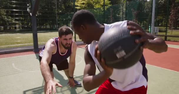 Двоє багатоетнічних баскетболістів, які грають разом на відкритому дворі, практикують атаку та оборонний трюк, відстежують постріл — стокове відео