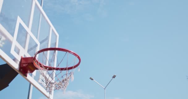 Meta y éxito. tiro al aire libre de pelota de baloncesto negro cayendo en el bucle de streetball sobre fondo de cielo azul — Vídeo de stock