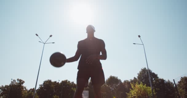 Silhouet van Afrikaanse amerikaanse basketbalspeler training buiten, gooien bal in hoepel, poseren over zon vlam — Stockvideo