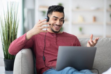 Neşeli orta doğulu adam evden çalışıyor, video konferansı yapıyor.