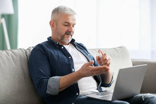 Reifer Mann benutzt Desinfektionsspray zum Reinigen der Hände mit Laptop — Stockfoto