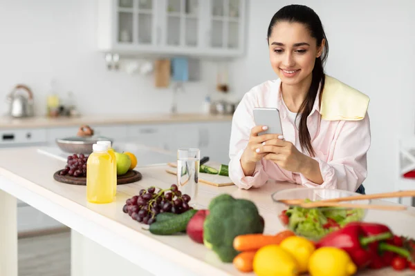 Porträt einer lächelnden jungen Frau, die ihr Handy in der Küche benutzt — Stockfoto