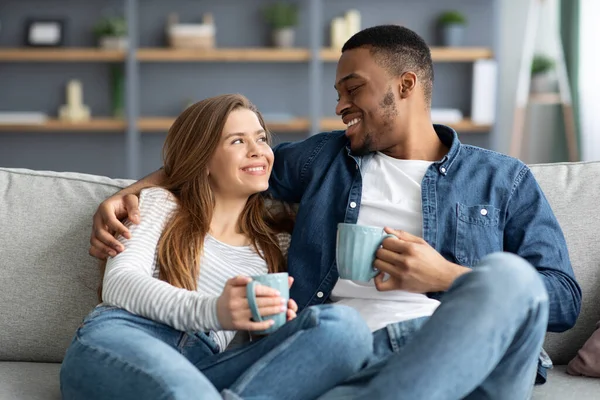 Wochenend-Pastime. Glückliches gemischtes Paar entspannt sich auf Couch mit Kaffee zu Hause — Stockfoto
