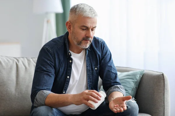 Senior man tar piller när du sitter på soffan hemma — Stockfoto