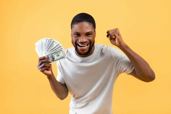 Alegre afroamericano hombre sosteniendo un montón de dinero, haciendo SÍ gesto sobre fondo de estudio amarillo — Foto de Stock