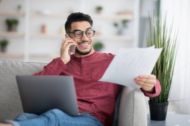 Bilgisayarı ve cep telefonunu kullanarak çalışan Ortadoğulu bir adam.