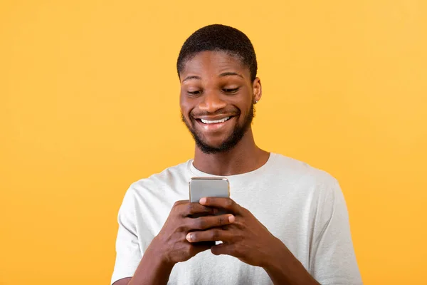 Ludzie i koncepcja technologii. Podekscytowany Amerykanin z Afryki za pomocą smartfona nad żółtym tle studio — Zdjęcie stockowe