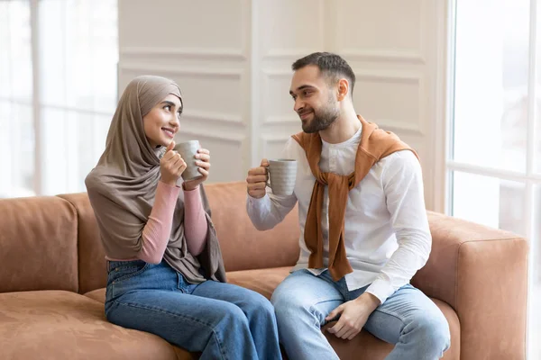 Fröhliche muslimische Ehepartner trinken Kaffee auf Couch im Haus — Stockfoto