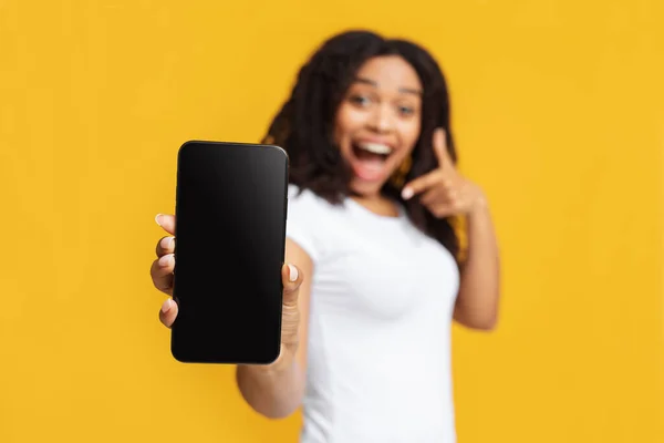 Cool new app. Excited black lady holding smartphone with blank screen in hand, showing device to camera — Stock Photo, Image