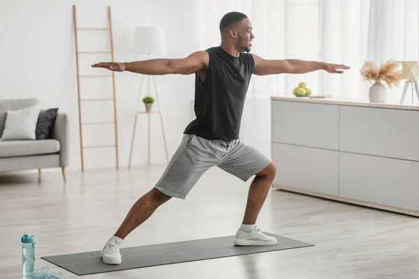 Hombre afroamericano haciendo yoga de pie en la posta del guerrero en interiores — Foto de Stock