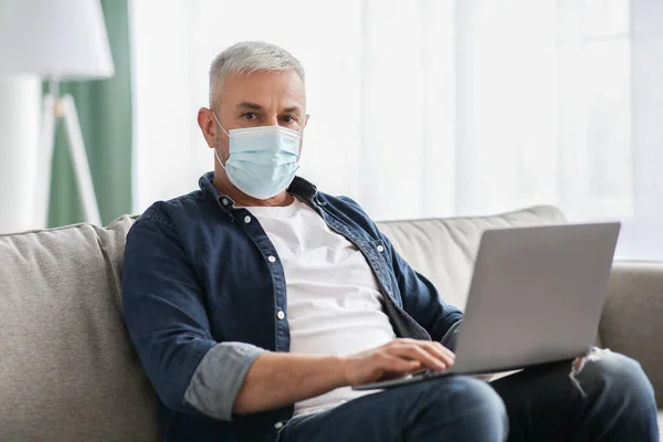 Старший человек в маске работает онлайн во время пандемии — стоковое фото