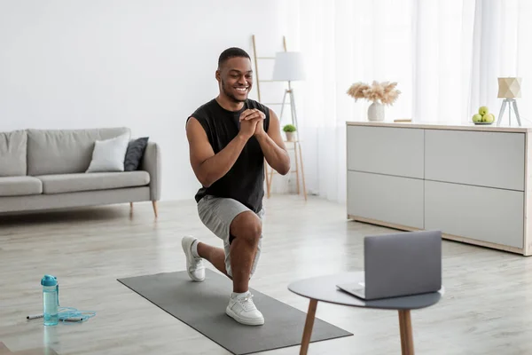 Hombre negro haciendo ejercicio de salto hacia adelante cerca de la computadora portátil en casa —  Fotos de Stock