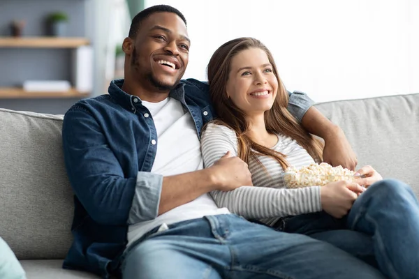 Encontro em casa. Casal interracial relaxante no sofá, assistindo TV e comer pipoca — Fotografia de Stock