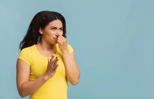 Mujer afroamericana tapándose la nariz, oliendo algo apestoso y desagradable sobre fondo azul, espacio para copiar —  Fotos de Stock