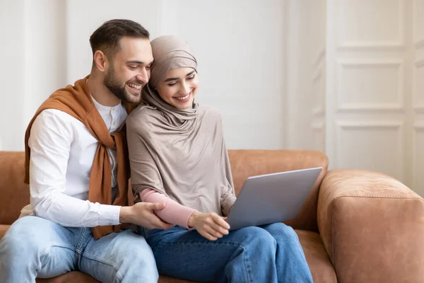 Fröhlich verheiratetes muslimisches Paar sitzt mit Laptop zu Hause — Stockfoto