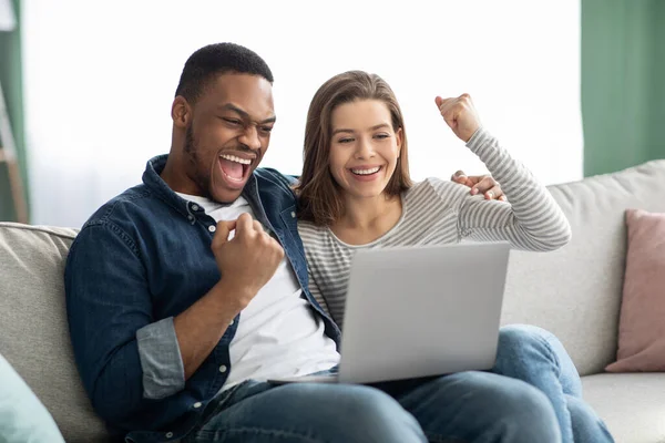 Feliz pareja Interracial Emocionado celebrando el éxito con el ordenador portátil en casa —  Fotos de Stock