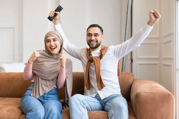 Emocional casal muçulmano balançando punhos assistindo TV em casa — Fotografia de Stock