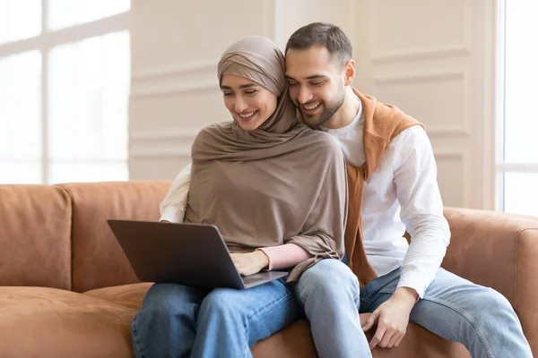 Sposi musulmani moderni che utilizzano il computer portatile guardando film insieme a casa — Foto Stock