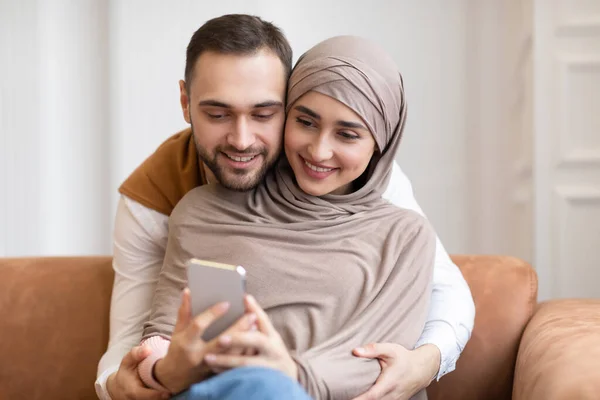 Casal muçulmano feliz usando telefone móvel juntos em casa — Fotografia de Stock