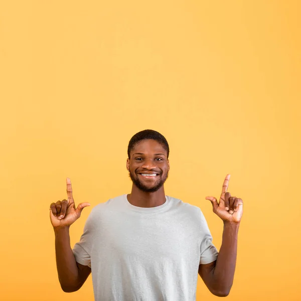 Concepto de venta o descuento. Emocionado chico afroamericano apuntando hacia arriba en el espacio vacío sobre fondo amarillo — Foto de Stock