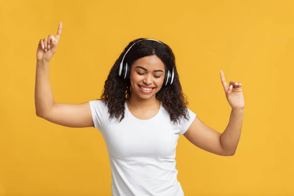 Dame afro-américaine insouciante dans les écouteurs datant de sa playlist préférée avec les yeux fermés sur fond de studio jaune — Photo