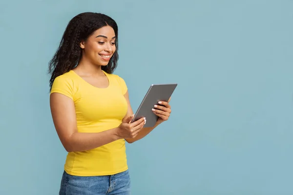 해피 아프리카계 미국 여성 디지털 태블릿에서 소셜 네트워크를 탐색하고 있는, 푸른 스튜디오 배경 위에 서 있는, 복사 공간 — 스톡 사진
