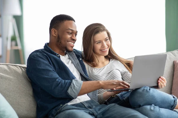 Retrato de feliz casal interracial relaxante com laptop na sala de estar — Fotografia de Stock