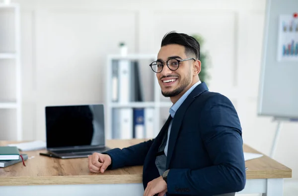 Feliz hombre de negocios árabe sentado en la mesa con ordenador portátil en la oficina de la empresa, maqueta para el diseño de sitios web — Foto de Stock