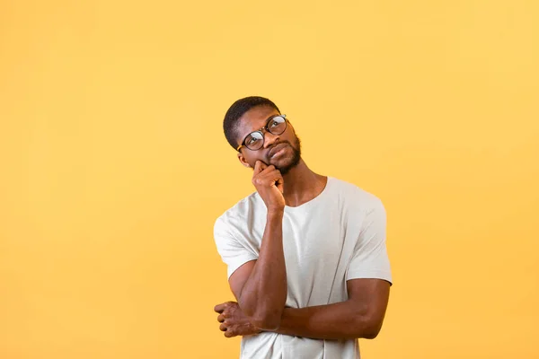 Sto cercando un'idea. Ragazzo afroamericano riflessivo guardando lo spazio libero, in posa su sfondo giallo — Foto Stock