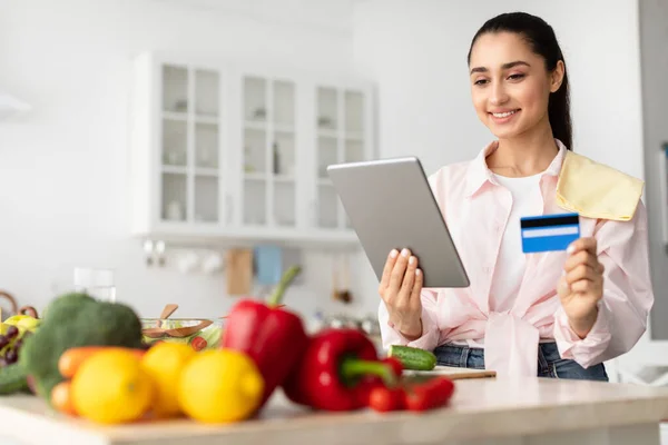 Woman shopping online using tablet and credit card in kitchen