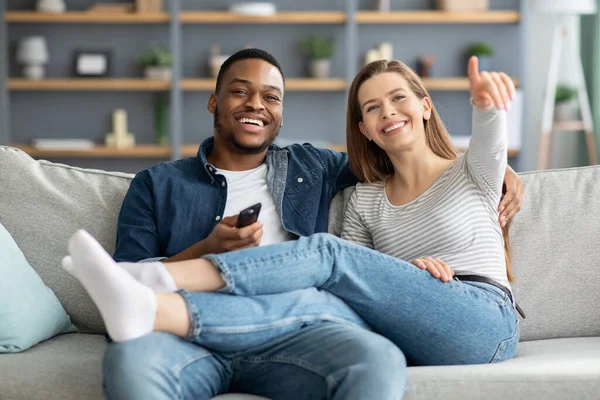 Felices amantes interraciales pasar tiempo en la sala de estar juntos, viendo la televisión —  Fotos de Stock