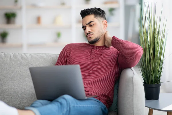 Junger Mann leidet unter Nackenkrampf, während er Laptop benutzt — Stockfoto