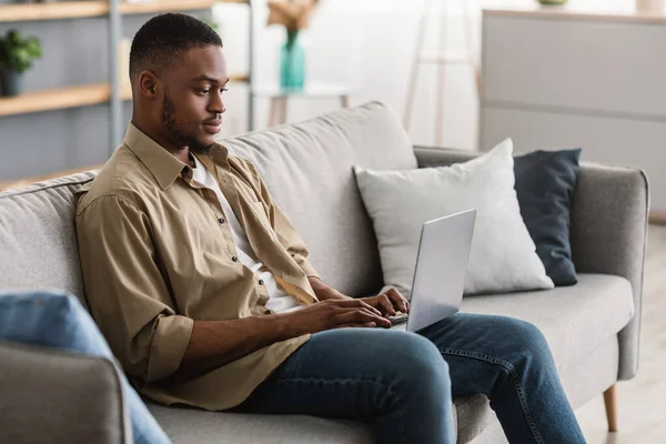 Serious Black Man Usando el Ordenador Portátil Navegando por Internet Sentado en Casa —  Fotos de Stock