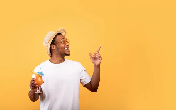 Impressionante oferta de verão. Homem afro-americano alegre com saboroso coquetel tropical apontando para o espaço vazio — Fotografia de Stock