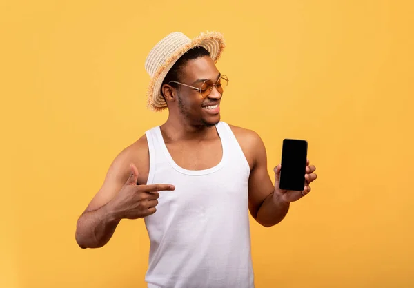 Funky fekete srác nyári ruhában mutat üres mobiltelefon felett sárga stúdió háttér, mockup design — Stock Fotó